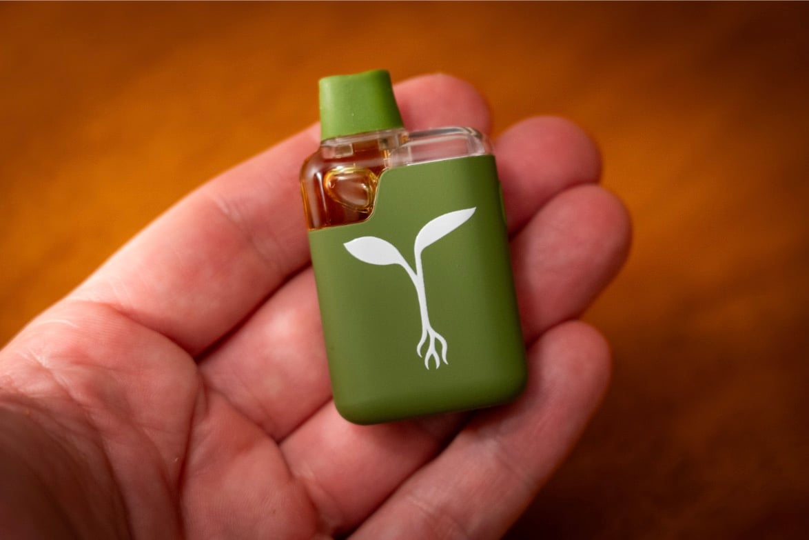 An image of a small disposable vape with a green case and mouth piece and visible oil in a clear container.
